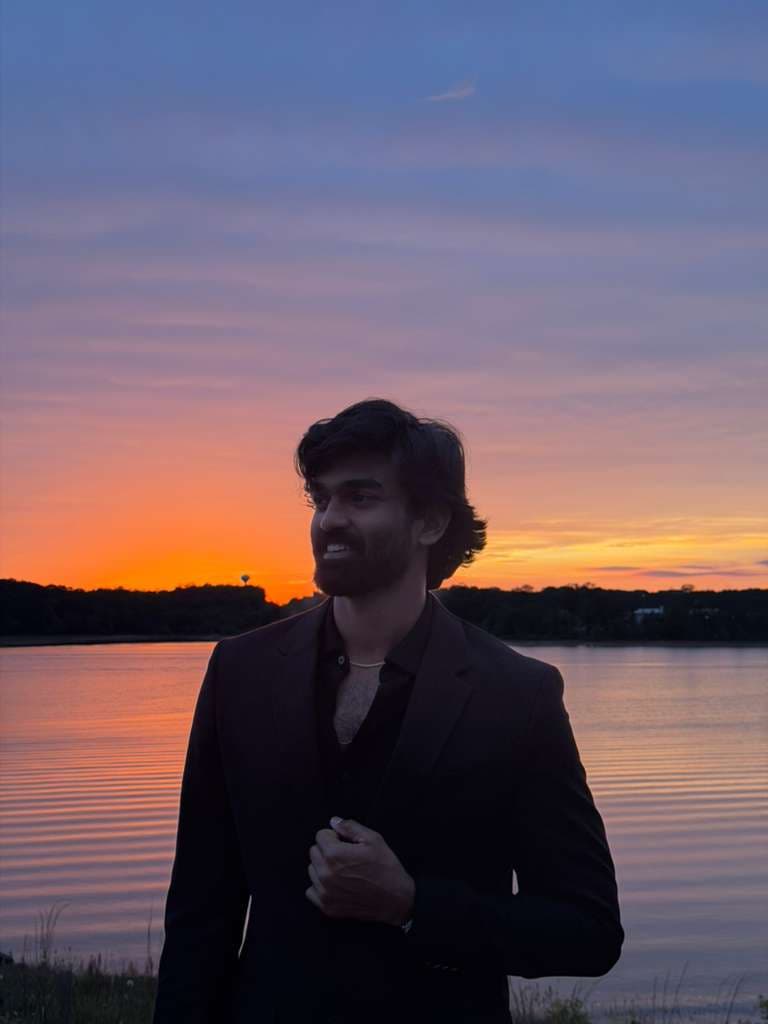 Ajay Chowdary Dodda in a suit by a lake at sunset
